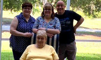 Carol sitting in a chair surrounded by her family outside on a sunny day