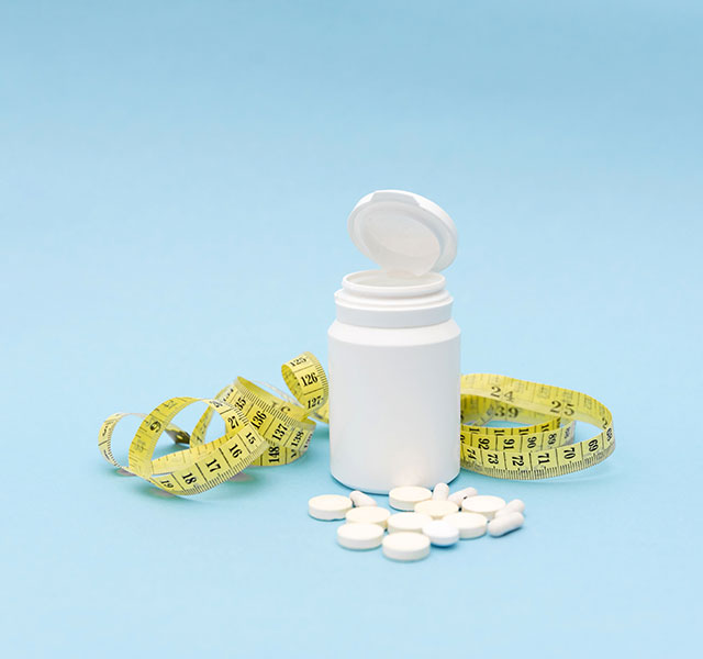 A white bottle with an open lid is on a light blue background, surrounded by a yellow measuring tape and several white pills scattered around the bottle. next generation weight loss meds